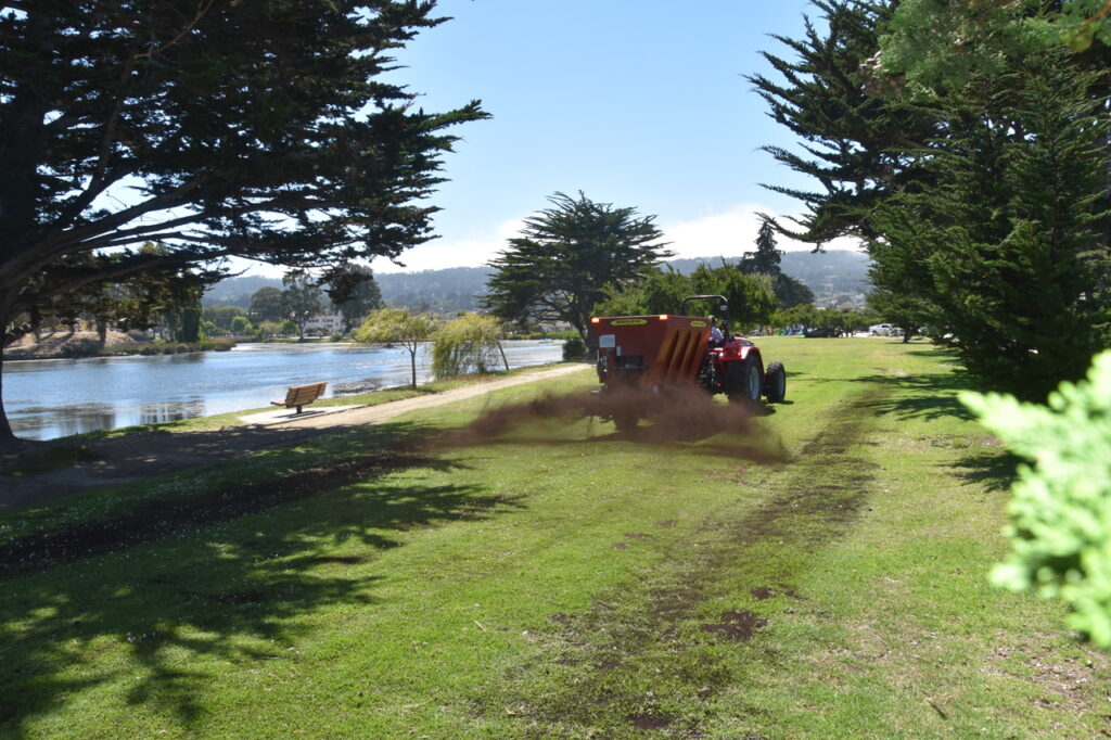 A tractor compost blower spreading compost on a park near water in Monterey, CA