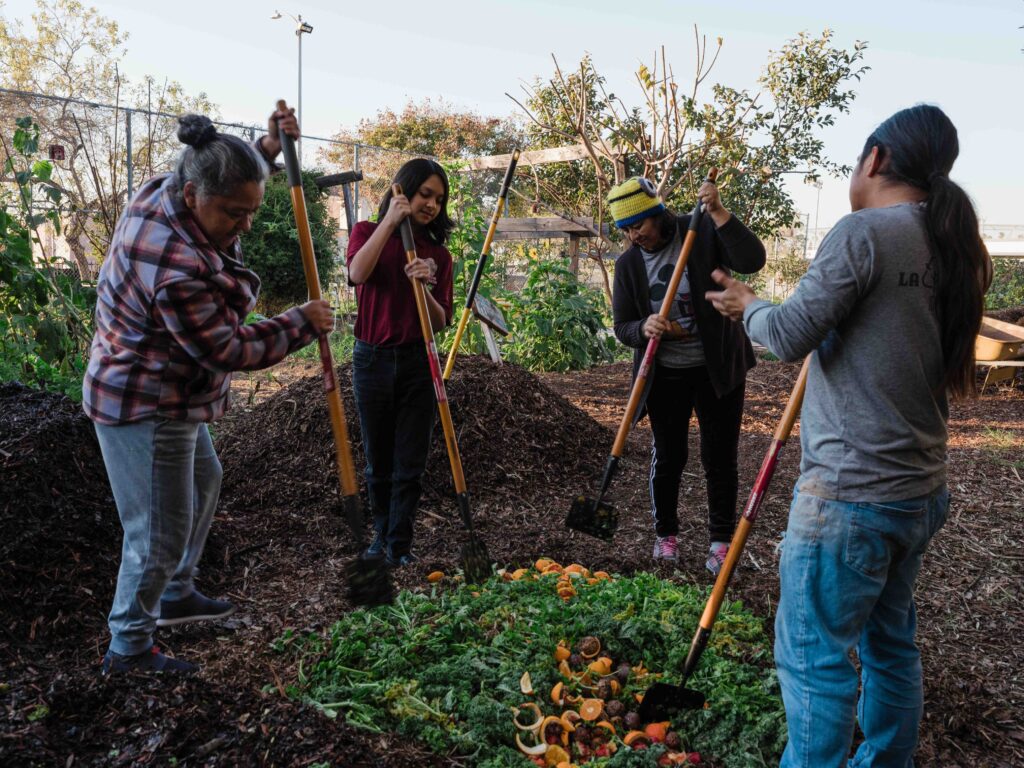Image of three volunteers and an LA Compost coordinator mixing in food scraps with woodchips, making compost